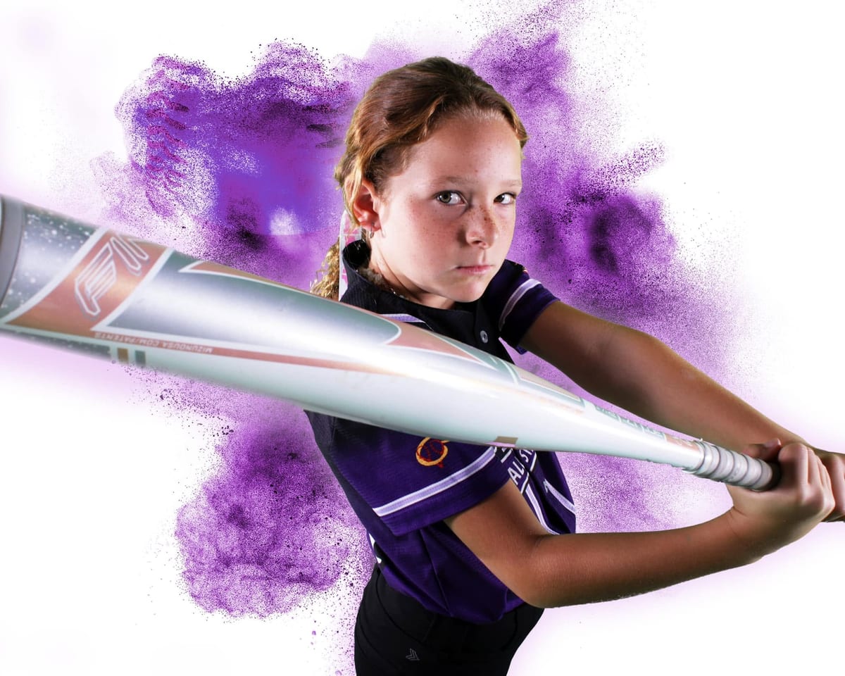 Softball player mid-swing against a purple powder burst