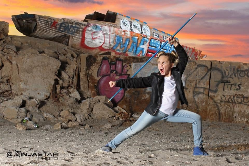 Young athlete posing with a staff against a graffiti wall at sunset